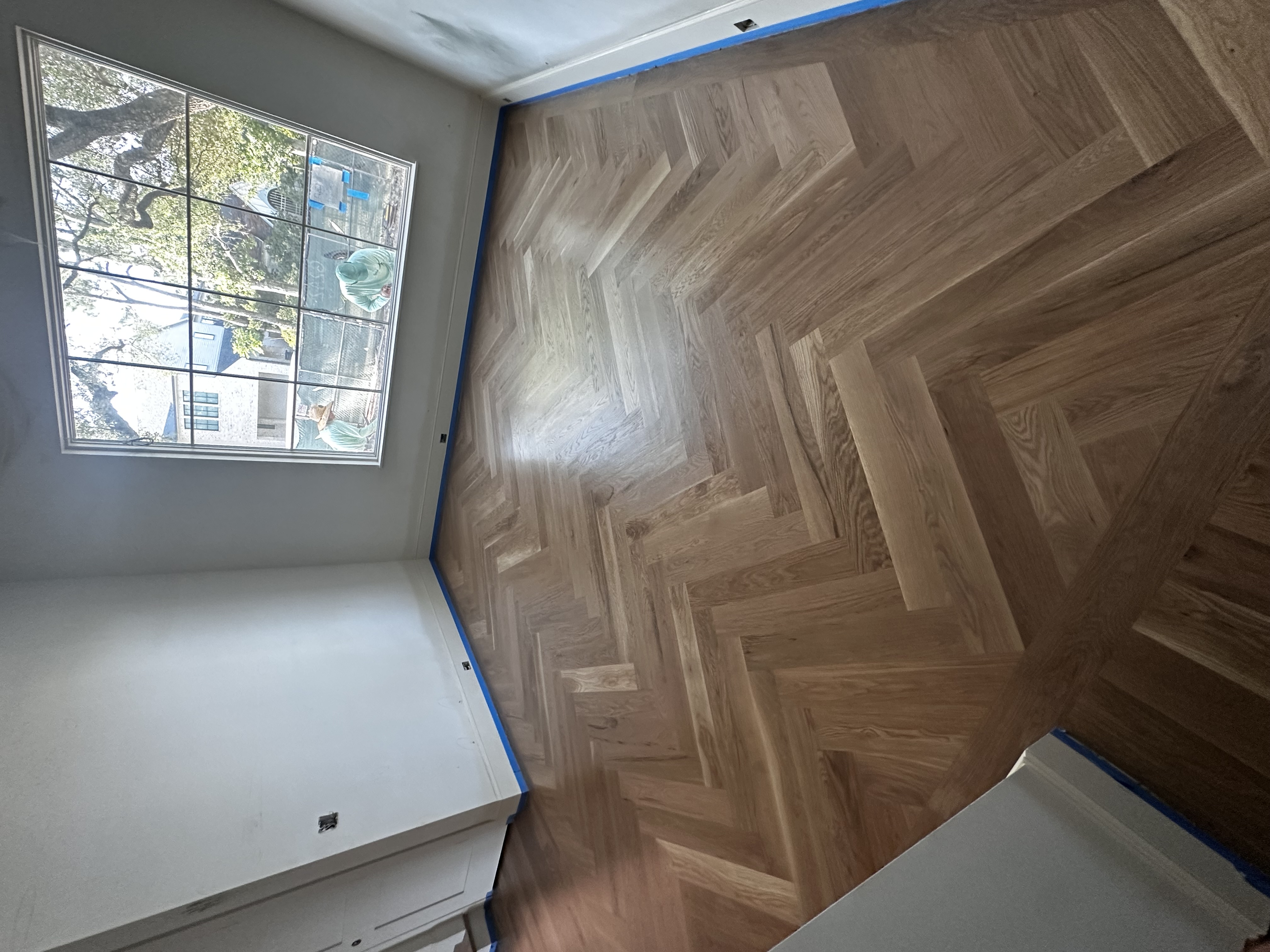 Natural raw herringbone white oak floor in a bedroom with a large window
